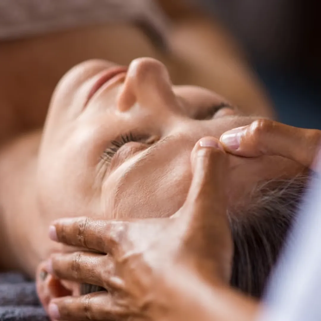 Personne recevant un massage du visage avec les mains appliquées sur le front, les yeux fermés en détente.