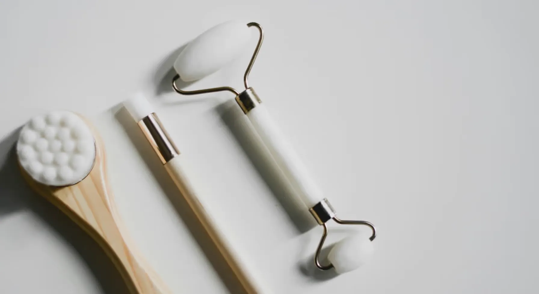 Ensemble d'outils de soin de la peau comprenant une brosse en bois, un rouleau de jade blanc à deux têtes et un stylo de massage facial blanc.