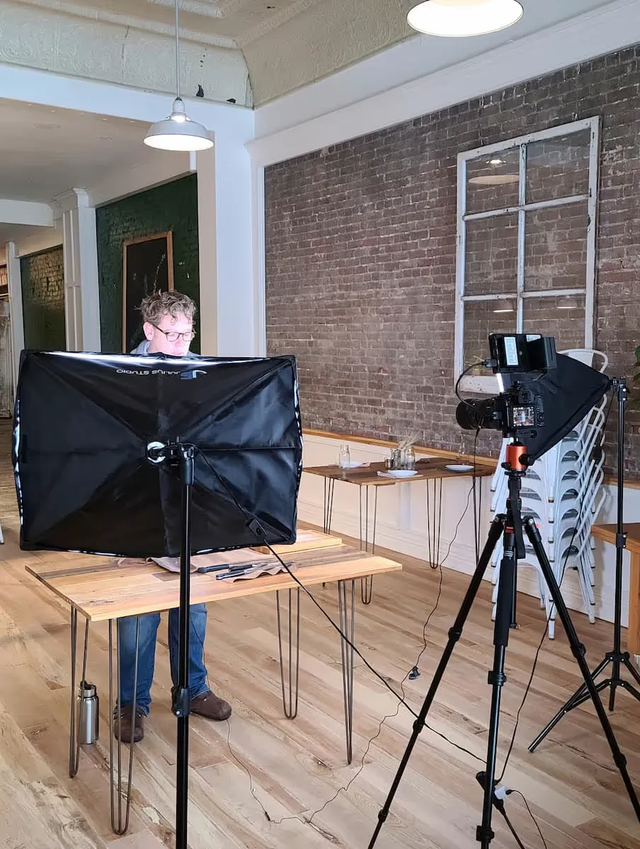 Un homme travaillant dans un studio photo avec un éclairage professionnel et un appareil photo sur trépied devant lui.
